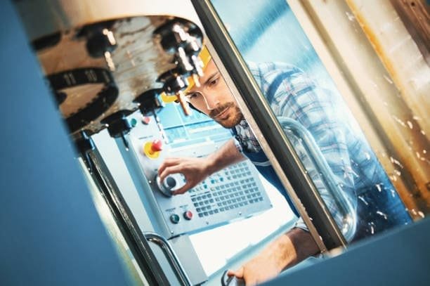 Engineer inspecting a CNC machine while adjusting the control settings, illustrating the machine setup and calibration stage of CNC operations.