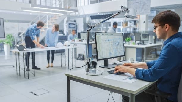 Engineer working on a CAD and CAE-integrated software while team members collaborate in the background, illustrating modern engineering workflows powered by computer-aided engineering.