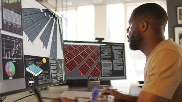 Engineer working on dual monitors with solar panel schematics and data visualizations, illustrating advanced applications of computer-assisted design in renewable energy systems.
