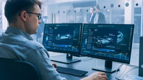 Engineer working on dual monitors displaying automotive component simulations, demonstrating the use of computer-assisted design in vehicle development and testing.
