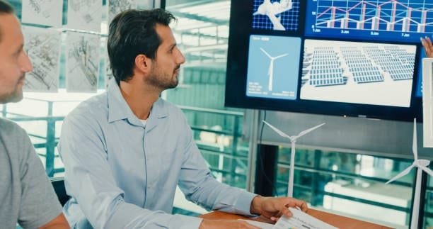 Engineer reviewing wind turbine and solar panel layouts on a digital screen, showcasing the use of computer-assisted design in sustainable energy system planning.