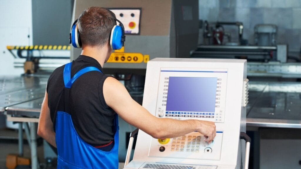 CNC machine operator adjusting settings on a computerized CNC control panel in a manufacturing facility.