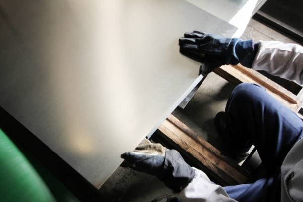 Worker handling a metal sheet before loading it into a CNC machine, illustrating the material setup stage in CNC machining processes.