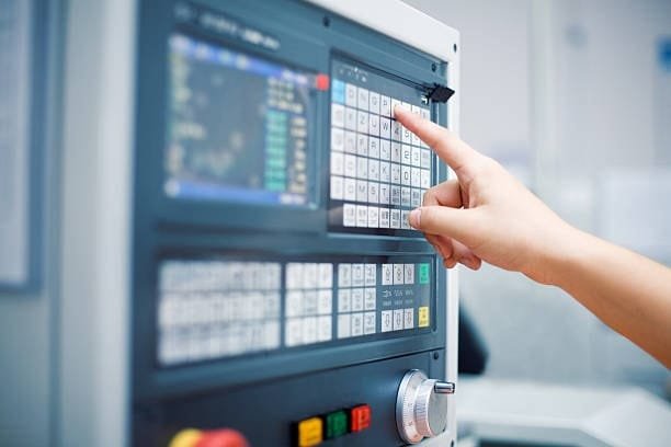 Operator hand programming a CNC machine through a detailed control panel interface.