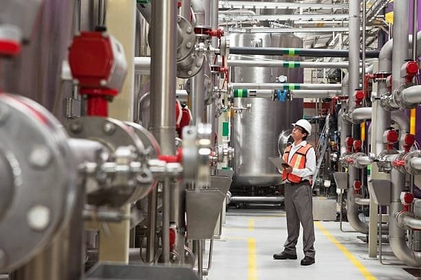 Worker conducting quality control inspection inside a large industrial processing facility.