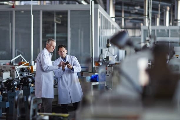 Two quality control engineers in lab coats examining manufactured components in a factory.