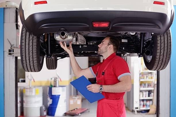 Technician inspecting a car’s underbody during vehicle quality control inspection.