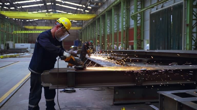Worker cutting steel beams using a circular saw and wearing safety gear.