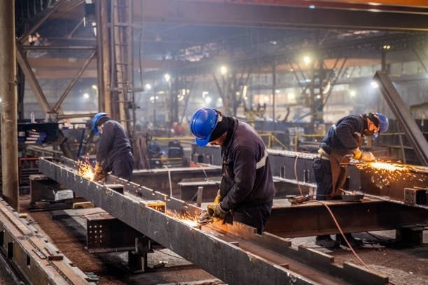 Industrial workers cutting large metal beams with circular saws in a factory.