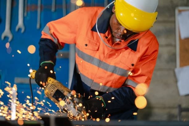 Worker using a manual grinder to cut metal, producing bright sparks.