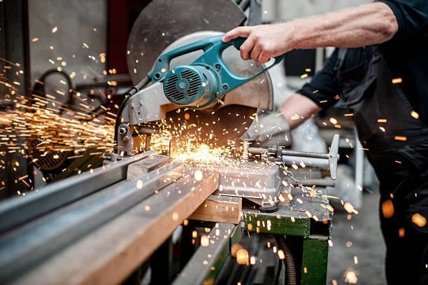 Circular saw used for cutting metal beams in a factory setting with sparks.