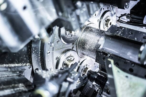 Multi-tool lathe machine simultaneously machining a cylindrical metal workpiece.