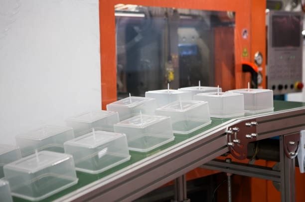 Plastic food containers moving along a conveyor belt in a plastic manufacturing facility.