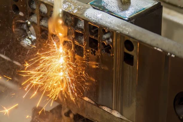 Sparks flying during wire EDM machining on metal component.
