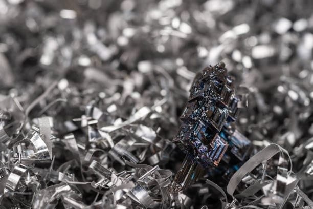 A blue-purple bismuth crystal placed among sharp curled steel machining chips