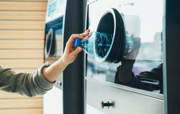 Person recycling a plastic bottle at a reverse vending machine as part of the plastic reuse cycle