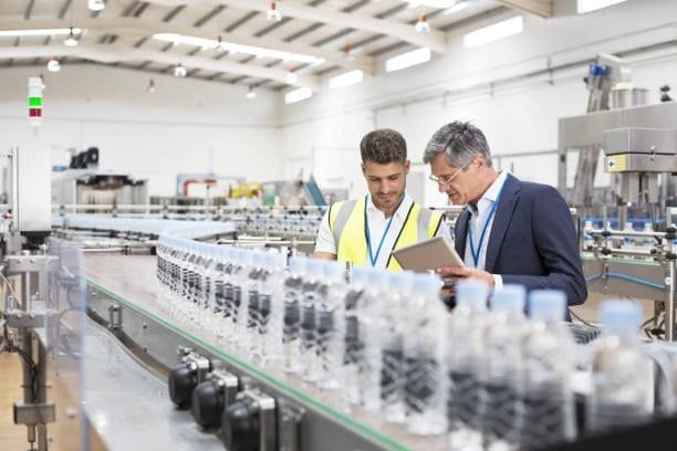 Two professionals inspecting a conveyor line of plastic bottles in a molding factory