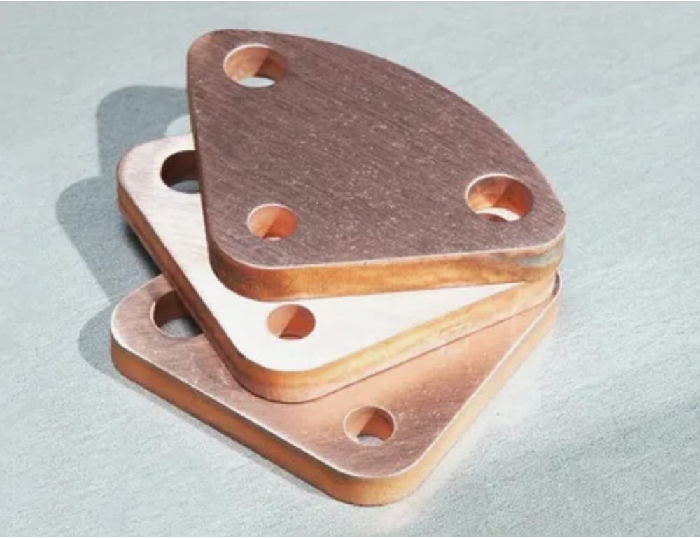 Stack of triangular copper sheet metal cutouts featuring four evenly spaced bolt holes