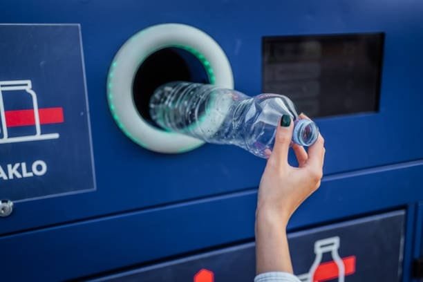 Close-up of a person inserting a plastic bottle into a reverse vending recycling unit
