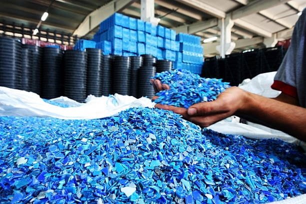 Hands holding blue shredded plastic above a large pile of purple plastic flakes