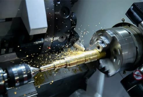CNC lathe cutting a metal shaft with live tooling, producing golden metal chips