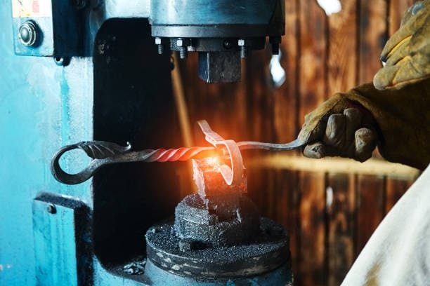 Artistic metal twisting being done under blue forging press