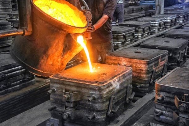Worker pouring molten metal into multiple molds at an industrial foundry