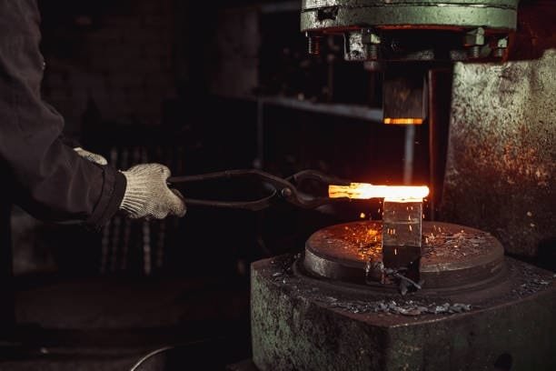 Red-hot metal billet being forged on industrial hammer press