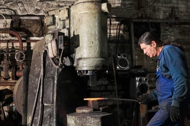 Blacksmith using industrial forging press to shape metal bar
