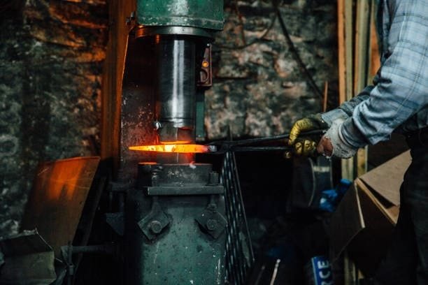 Red-hot steel being shaped using a mechanical hammer forging machine