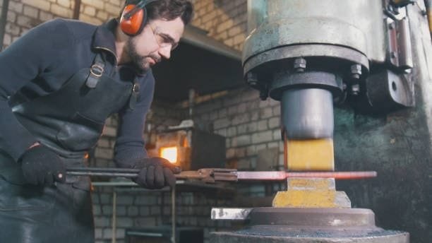 Worker using hydraulic forging press to shape hot metal