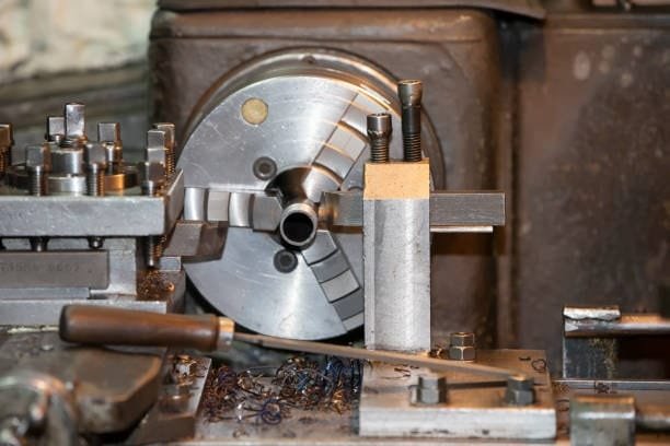 Metal workpiece clamped inside a lathe chuck with various manual tools nearby.