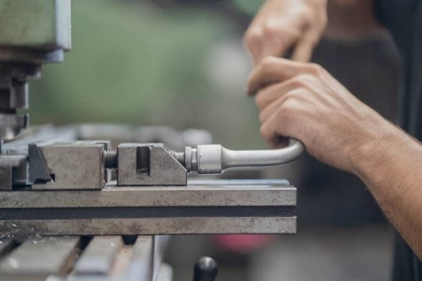 Operator adjusting the vice on a manual lathe machine, preparing for metal turning.