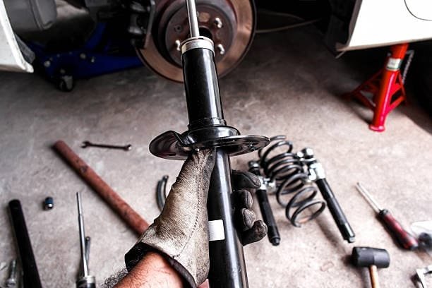 Technician holding removed automotive shock absorber for inspection or replacement