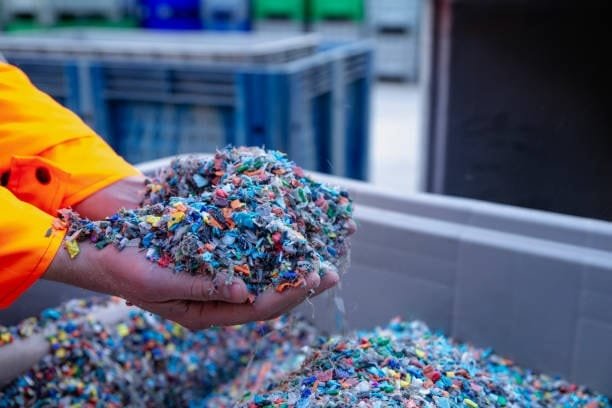 Gloved hands holding colorful shredded recycled plastic material in a bin