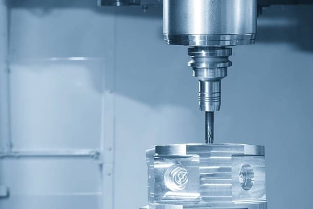 Vertical CNC milling head performing a precise operation on a metal block in a multi-axis setup.
