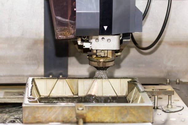 Wire EDM head submerged in fluid while cutting a metallic component