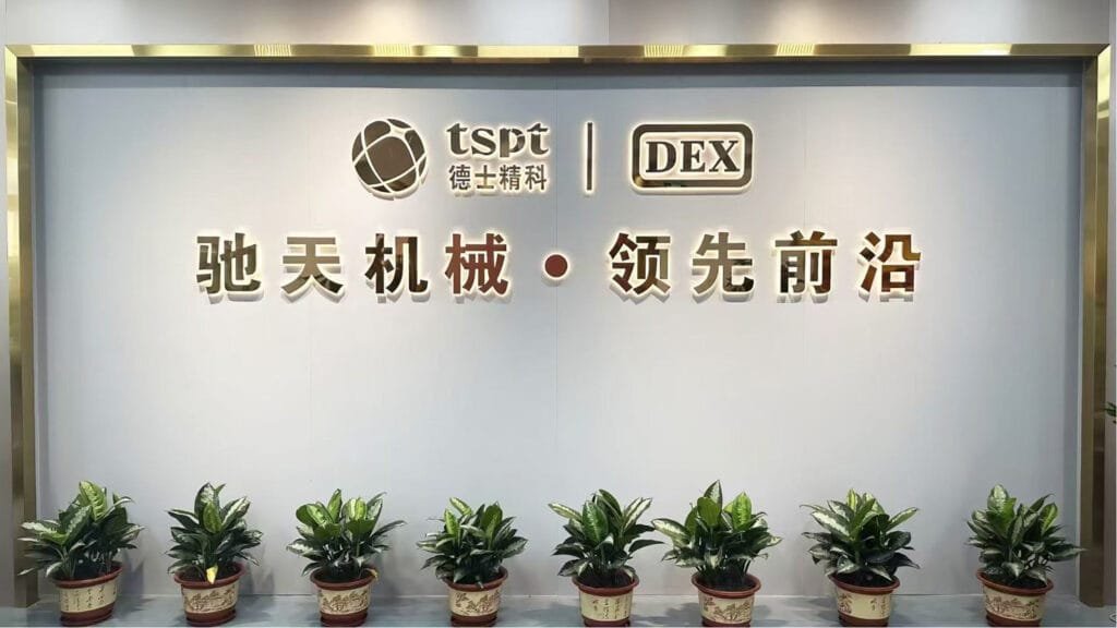 Reception wall sign displaying “TSPT 德士精科 | DEX 驰天机械 · 领先前沿” with a row of potted plants beneath.